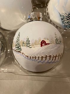 three christmas ornaments are sitting on the counter top, one has a barn and snow covered field painted on it