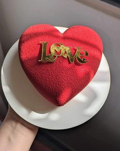 a red heart shaped cake with the word love on it sitting on top of a white plate