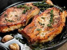 two pork chops in a cast iron skillet with garlic and cloves