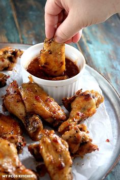 a person dipping sauce onto chicken wings on a plate