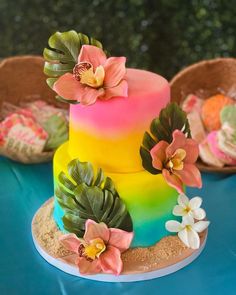 a multi - colored cake with flowers and leaves on the top is sitting on a blue table