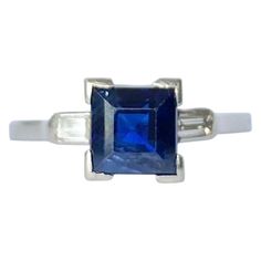 At the centre of this three stone ring there is a gorgeous deep blue sapphire and sat either side is a bright baguette diamond. The square cut sapphire measures 1ct and the diamonds measure 5pts each. Ring Size: K or 5 1/4 Height Off Finger: 5.5mm Weight: 2.5g Luxury Square-cut Brilliant Sapphire Ring, Luxury Square-cut Sapphire Ring With Brilliant Cut, Luxury Square Cut Brilliant Sapphire Ring, Classic Gia Certified Rectangular Sapphire Ring, Square-cut Brilliant Sapphire Ring, Rectangular Sapphire Ring With Accent Stones, Square Cut Brilliant Sapphire Ring, Classic Rectangular Sapphire Ring, Gia Certified Blue Square Cut Ring