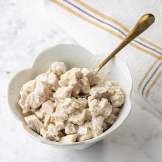 a white bowl filled with chicken salad on top of a counter next to a towel