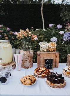 a table topped with lots of desserts next to flowers and jars filled with drinks