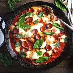 a pizza in a pan with basil leaves on the side and silverware next to it