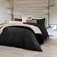 a bed with black comforter and pillows in a bedroom next to a wooden wall