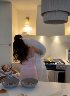 a woman in a pink dress standing next to a baby on a white counter top