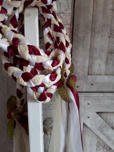 a red and white wreath hanging on the side of a wooden door with ribbon around it