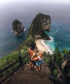 two people are standing on the stairs overlooking the water and cliffs in front of them