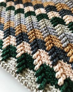 a crocheted blanket is laying on top of a white tablecloth with green, brown and tan colors