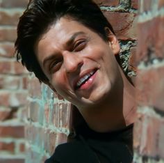 a young man is smiling and leaning against a brick wall with his head tilted to the side