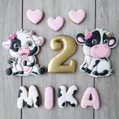 two decorated cookies in the shape of cows and hearts on a wooden table with numbers 2 - 4