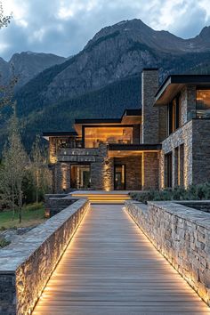 a wooden walkway leading to a house with stone walls and mountains in the background at night