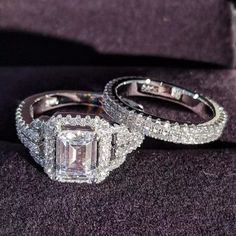 two wedding rings sitting on top of a purple velvet surface with diamonds around them and an emerald cut diamond in the middle