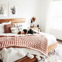 a bedroom with white walls and wooden bed frame, pillows and blankets on the headboard