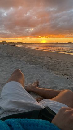 a man laying on top of a beach next to the ocean under a cloudy sky