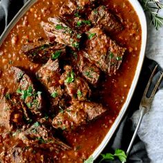 beef stew in a white dish with herbs on top and spoons next to it