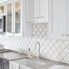 a kitchen with white cabinets and marble counter tops, along with an ornate tile backsplash