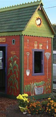 a small red and green building with potted plants on the outside, next to a fence