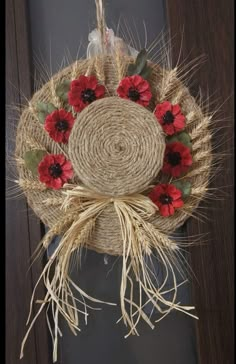 a wreath with red flowers hanging from the side of a wooden door, decorated with jute