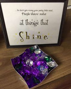 a box filled with purple and green candy next to a sign that says people throw rocks at things that shine