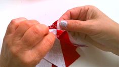 two hands are holding red and white paper with silver glitters on them, while another hand is wrapping the edge of an origami