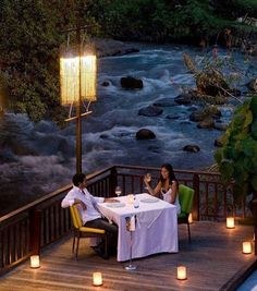 two people sitting at a table on a deck with lit candles in front of them