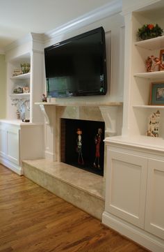 a flat screen tv mounted on the wall above a fireplace in a room with wooden floors