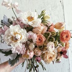 a bouquet of flowers is being held by someone's hand in front of a white wall