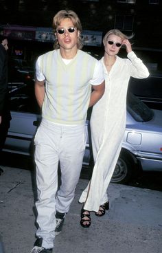 a man and woman walking down the street in front of some parked cars at night