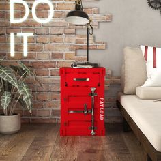 a red cabinet sitting on top of a wooden floor next to a white couch and brick wall