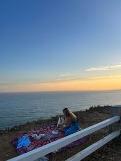 a woman sitting on top of a blanket next to the ocean