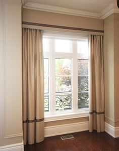 an empty room with wood floors and white curtains on the window sill, in front of a wrought iron fence