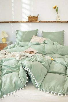 an unmade bed with green sheets and pom poms