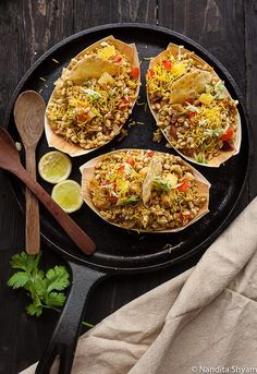 three tacos on a plate with limes and cilantro next to it