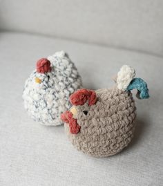 two crocheted chickens sitting next to each other on top of a white couch