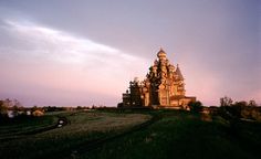 an old building sitting on top of a lush green field under a blue sky with clouds