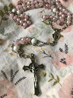 "This Small Ice Pink ladder rosary is made with ice pink glass rondelle 6mm beads  and white marble round glass 6 mm  beads. The rosary is connected with a beautiful Mary center piece made in Italy and finished with a Flared St Benedict crucifix. Ladder Rosaries, called such for their ladder-like design, are constructed to distribute the stresses of use from the eye pins and the beads, to the strong, durable chains which run, unbroken, through the length of the beads. This design adds tremendous strength and durability which has survived the rigors of both my husband's pockets and daily use, and the varied, impressive, physical contortions of our 3, and 5-year-old boys as they test their own strength against mommy's Rosary making prowess.   All our Rosaries are made with stainless steel ch Affordable Handmade Pink Rosary, Rosary Making, Mcbling Fashion, Dope Jewelry Accessories, Pearl Rosary, St Benedict, Saint Benedict, The Rosary, Dope Jewelry