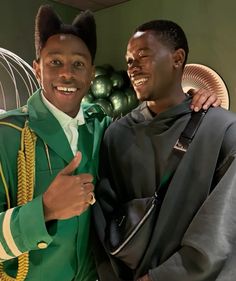 two men standing next to each other in front of green and gold decorations on the wall