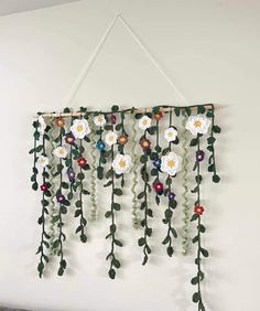 a wall hanging made out of flowers and leaves on a white wall next to a bed