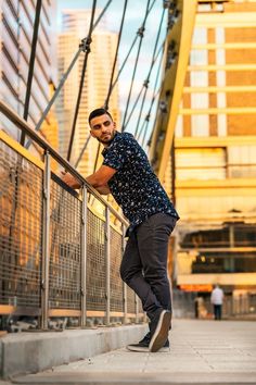 a man leaning against a railing in front of some tall buildings with his hand on the rail