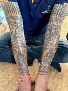 a man is sitting on the floor with his legs covered in tattoos and has one arm wrapped around another person's leg