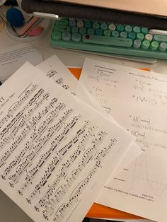 several sheets of music paper on a desk with a keyboard and calculator in the background