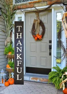 a front porch decorated for thanksgiving with pumpkins and greenery on the steps, wreathed door hanger