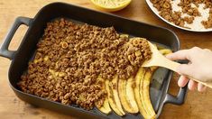 a person spooning food out of a pan with bananas and other foods on the table