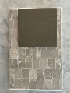 a white marble frame with a black square in the middle on a gray and white marble countertop