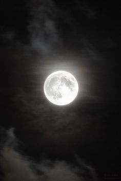 the full moon is seen through clouds in this black and white photo, with only one light visible