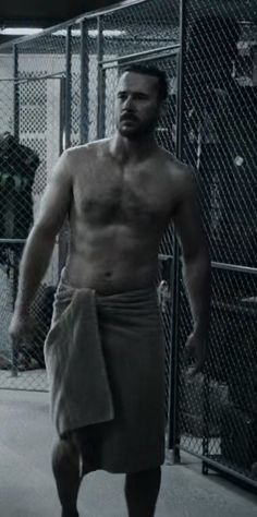 a man with no shirt on standing in front of a fence and holding a towel