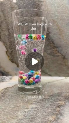 a glass filled with colorful beads on top of a counter next to a stone wall