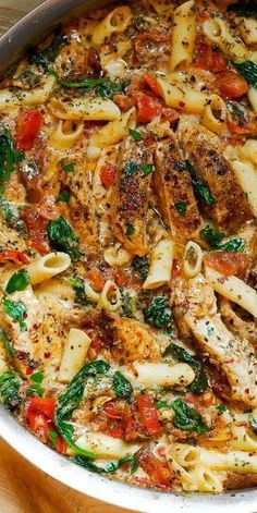 pasta with chicken, spinach and tomatoes in a skillet on a wooden table